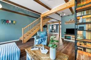 A spacious living room with a wooden staircase, a blue armchair, and a wooden coffee table with a vase of flowers. - "luxuriöser Aufenthalt in der Wohnung "hummer" auf dem Majorshof" (Hedwigenkoog)