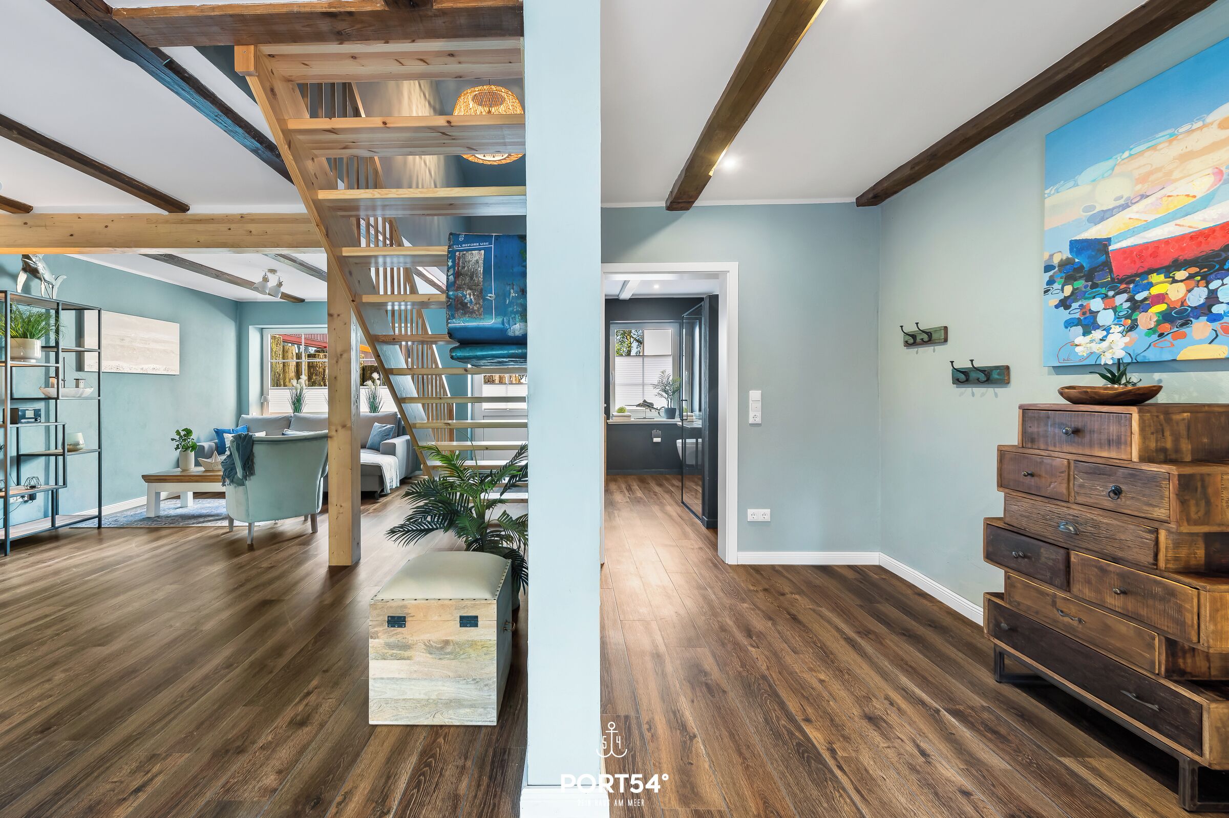 A spacious living area with a wooden staircase, a blue accent wall, and a large painting.