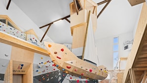 Eine Kletterwand mit verschiedenen Griffen und Holzbalken in einem Raum mit weißen Wänden und einem Fenster.