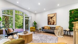Ein modernes Wohnzimmer mit großem Fenster, einer Couch, einem Couchtisch und einer grünen Wandgestaltung.