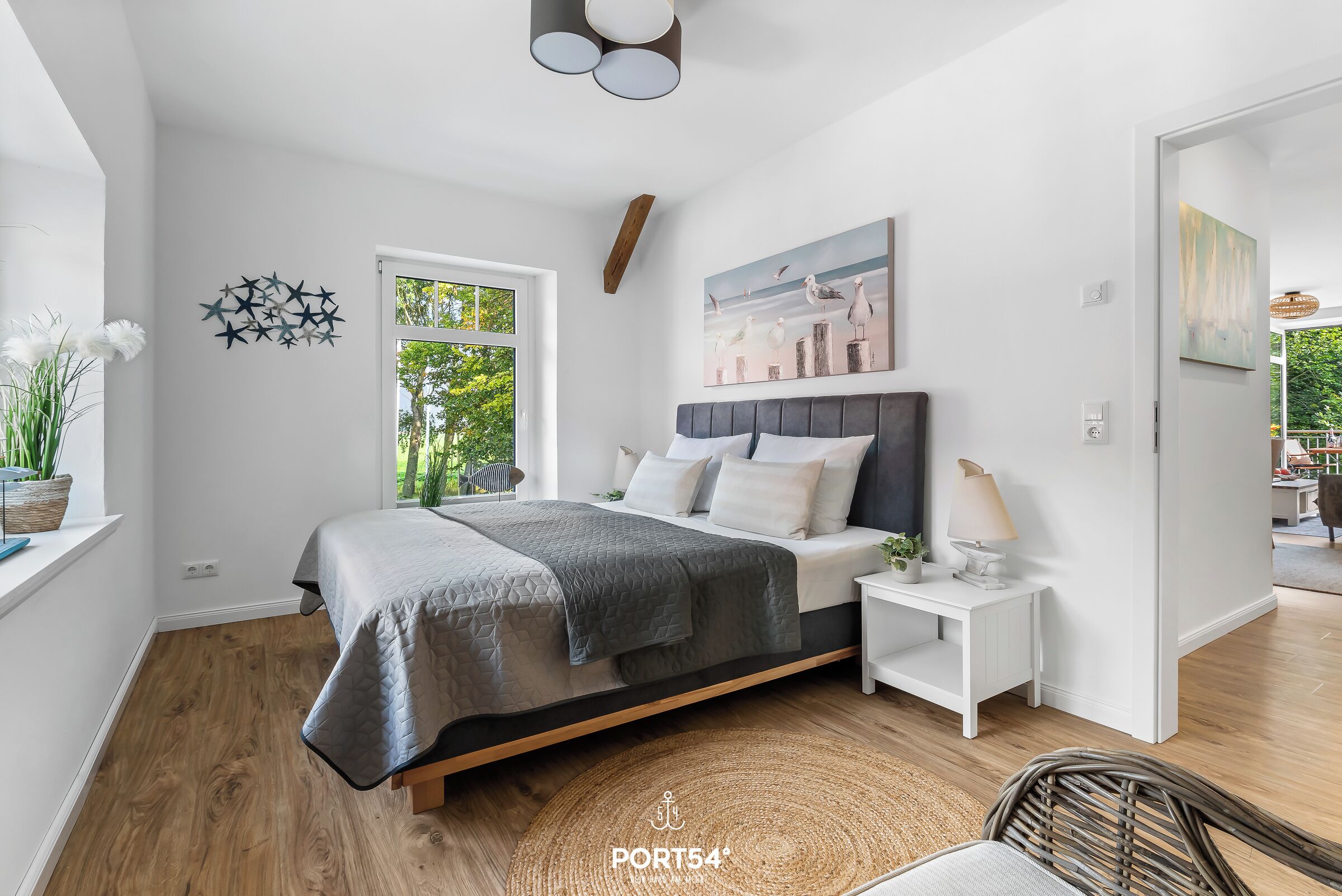 A modern bedroom with a bed, bedside tables, a window, and artwork on the wall.