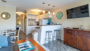 A modern kitchen with white cabinets, a central island, bar stools, and a flat-screen TV mounted on the wall.