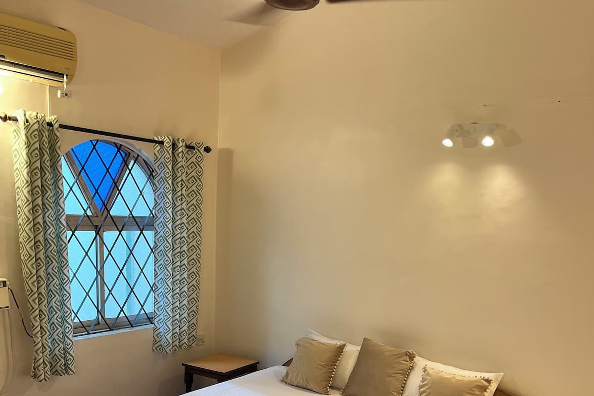 Un dormitorio con cama de madera, cortinas estampadas, ventilador de techo y ventana con vistas.