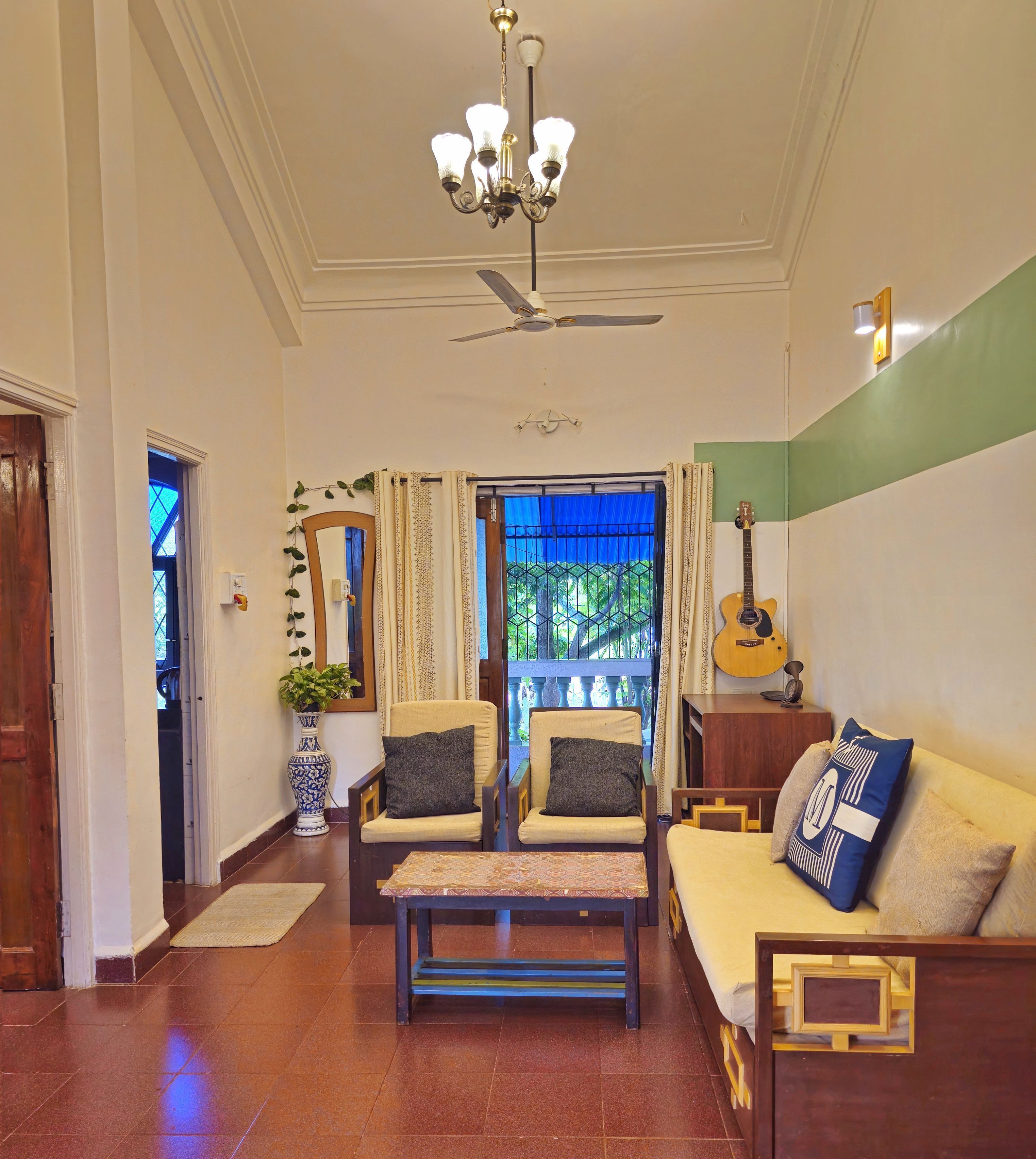A room with a ceiling fan, a chandelier, a guitar, and a sofa with cushions.