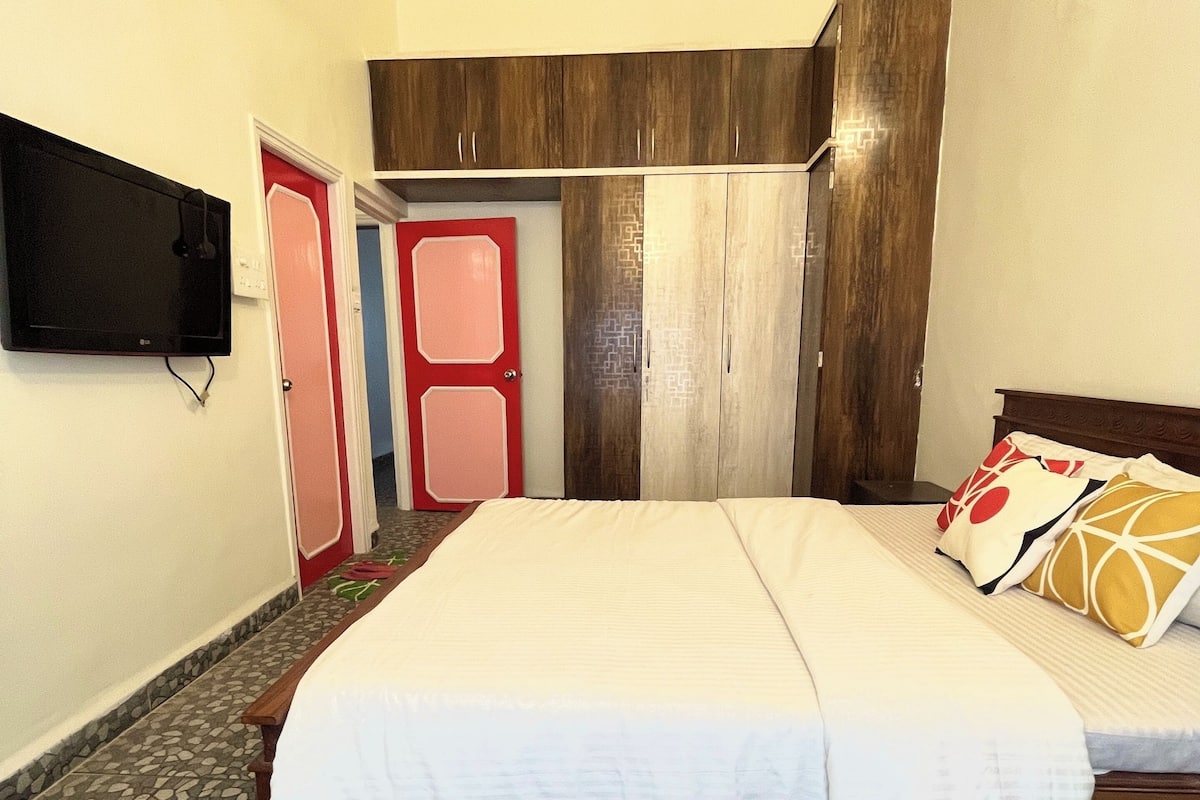 Un dormitorio con cama, ventilador de techo, televisor montado en la pared y armario.