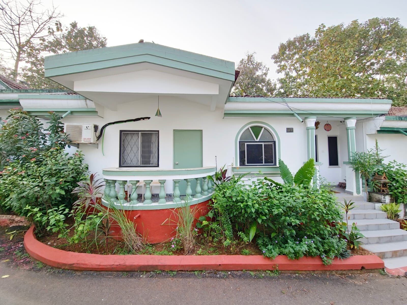 A two-story house with a green roof, a balcony, and a small garden area.