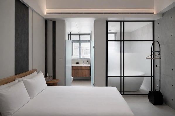 Un dormitorio moderno con cama, vestidor y baño con bañera.