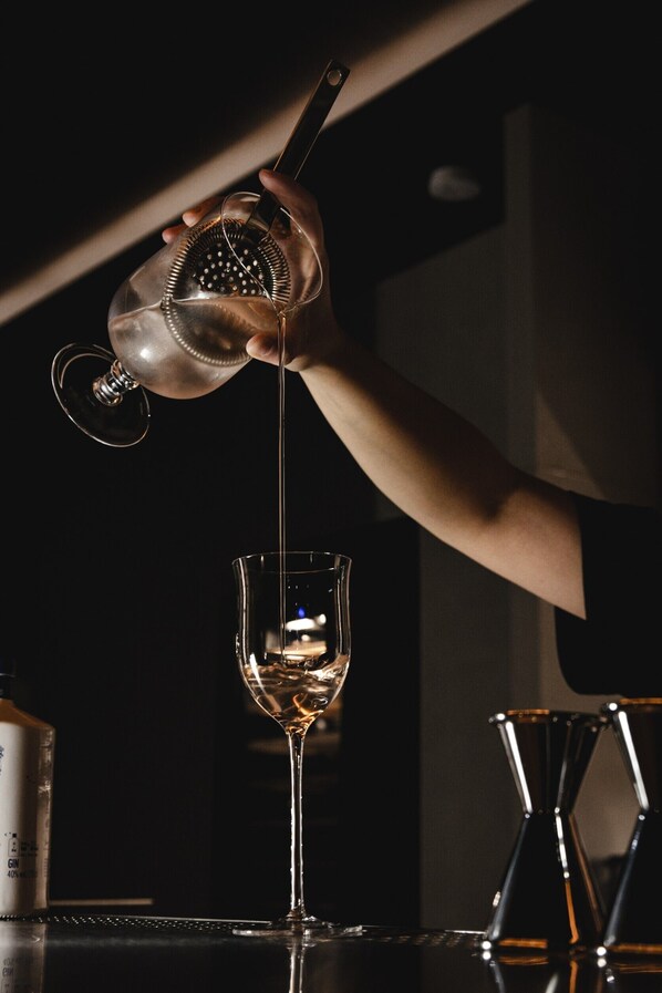 A hand pouring a clear liquid from a shaker into a tall glass. - Guangfa Hotel (Tainan)