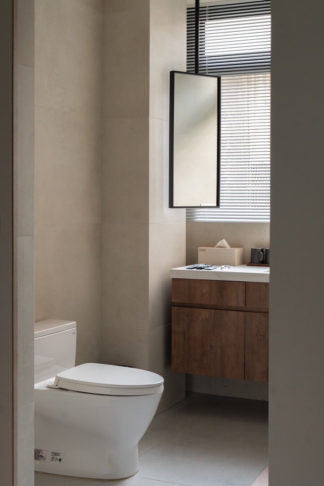 A modern bathroom with a toilet, a wooden vanity, and a large mirror.