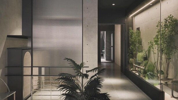 A modern interior with a central staircase, a glass partition with vertical lines, and a plant in the foreground. - Guangfa Hotel (Tainan)