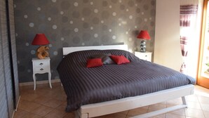 Une chambre à coucher avec un lit, deux tables de chevet, une lampe rouge sur chacune, et un papier peint à pois.