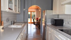 Une cuisine avec des armoires blanches, un évier, une cuisinière et un four à micro-ondes. On aperçoit une chaise et une table au fond.