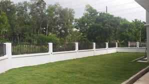 Un mur blanc avec une clôture en métal noir, une pelouse bien entretenue et, au fond, de grands arbres aux feuillages denses.