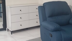 Une chambre moderne avec une commode blanche, une chaise bleue et un grand miroir au mur.