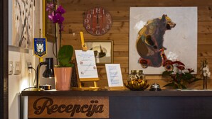 A reception desk with a sign reading "Recepcja," a clock, a framed picture of a bear, and various decorative items including a potted plant and a flower arrangement. - B&B Plitvice Queen (Plitvicka Jezera)