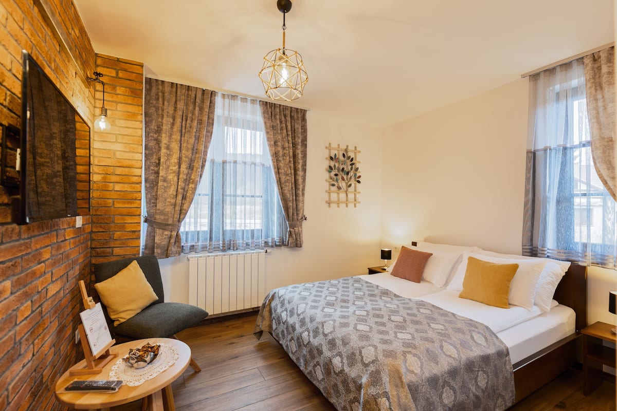 Una habitación de hotel acogedora con pared de ladrillo, cama con ropa de cama estampada, una mesita con un control remoto y una lámpara de pared.