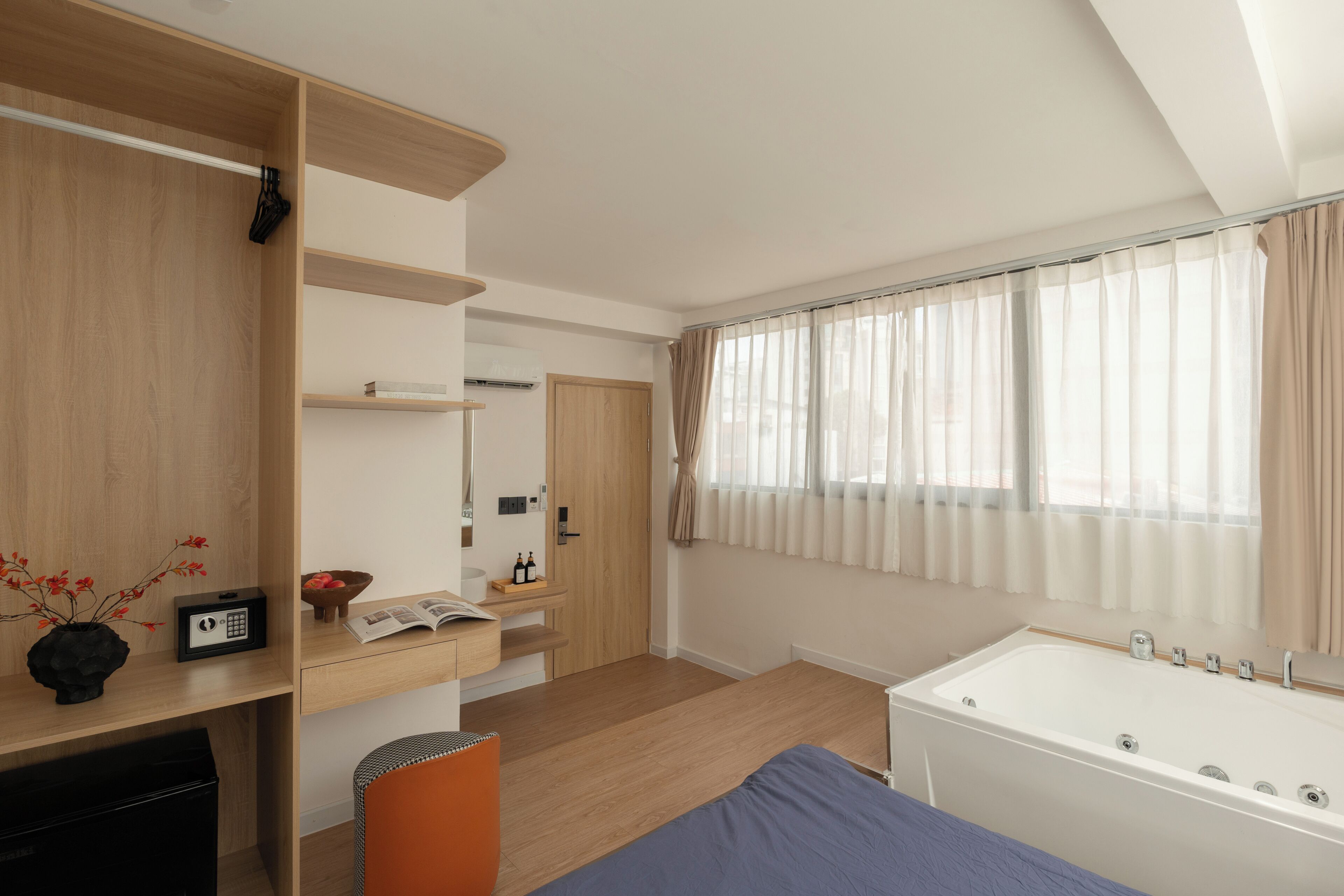 Une chambre moderne avec une armoire en bois, une table de chevet avec un livre et un vase, une grande fenêtre avec des rideaux et une baignoire blanche.