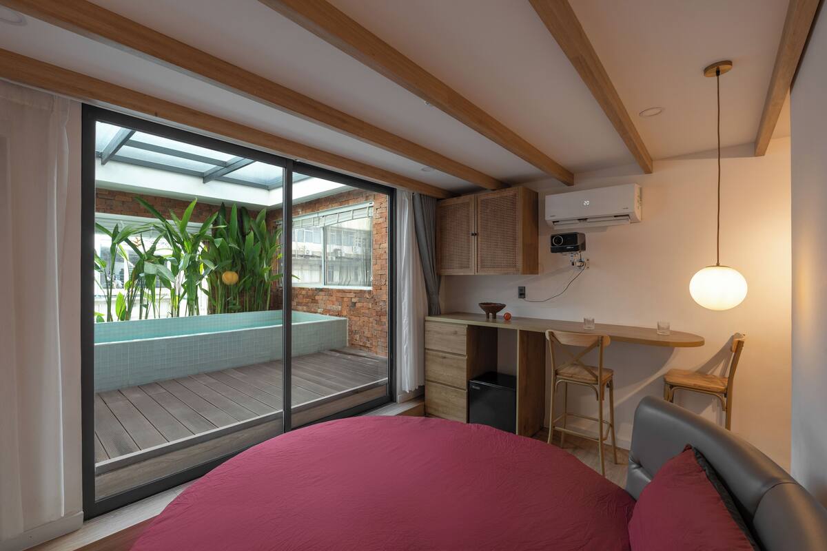 Une chambre moderne avec un grand lit, un bureau et une vue sur un balcon agrémenté de plantes.