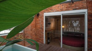 A pool area with a wooden deck, a glass door leading to a room with a red bed, and a brick wall. - Zeus Living Central Hotel (Ho Chi Minh City)