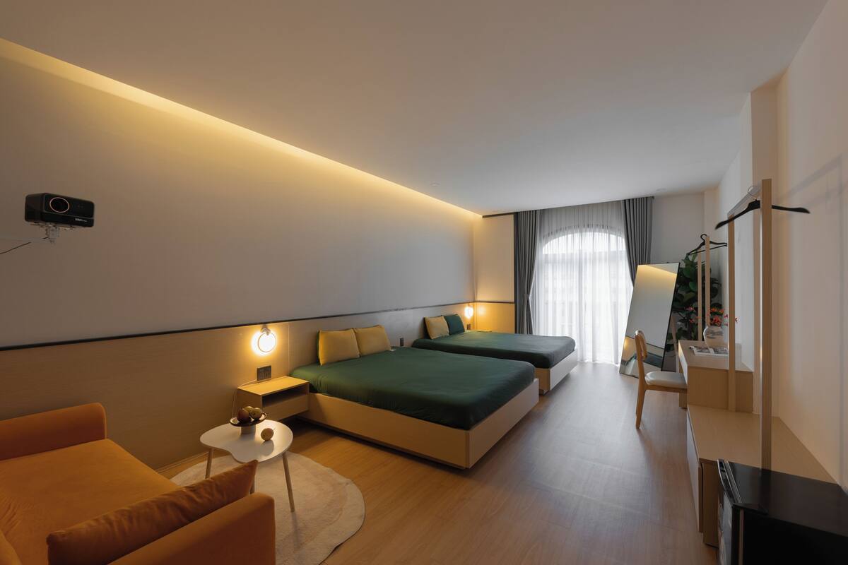 Une chambre d’hôtel moderne équipée de deux lits, d’un bureau, d’une chaise et d’un téléviseur à écran plat fixé au mur.