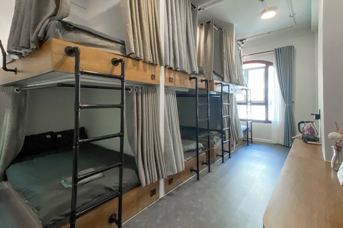 Une chambre de dortoir avec des lits superposés, un bureau en bois et une fenêtre avec des rideaux.