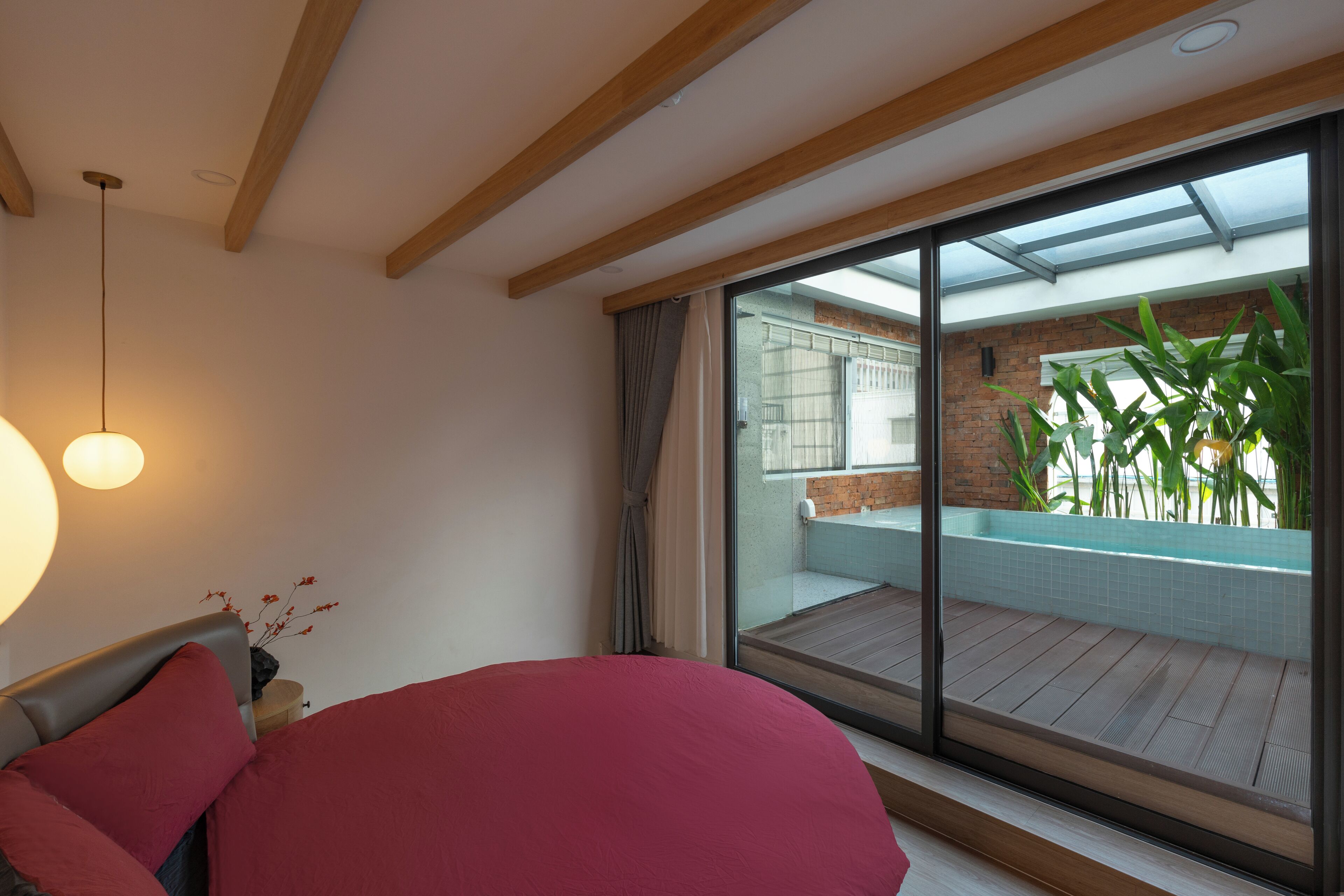 A bedroom with a large bed, a view of a balcony with a pool, and a modern interior design.