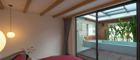 A bedroom with a large bed, a view of a balcony with a pool, and a modern interior design.
