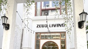 The exterior of Zeus Living, featuring a white facade, arched entrance, and outdoor seating area with steps leading up to the entrance. - Zeus Living Central Hotel (Ho Chi Minh City)