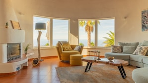 A living room with a fireplace, a sofa, a coffee table, and large windows with a view of palm trees.