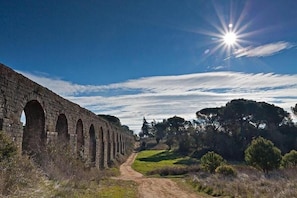 Un viaduc en pierre comportant plusieurs arches, un chemin de terre et un ciel dégagé où le soleil brille.
