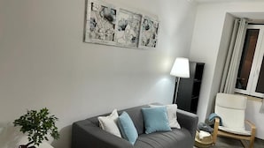 Una sala de estar moderna con un sofá gris, una mesita auxiliar con un bonsái, una lámpara y una silla blanca.