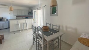 Een moderne keuken met witte kasten, een eethoek met een tafel en stoelen, en een hangende lamp.