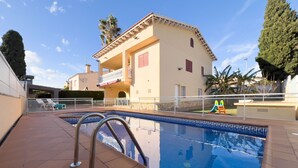 Une piscine avec une terrasse carrelée, une échelle en métal et un bâtiment doté d’un balcon en arrière-plan.