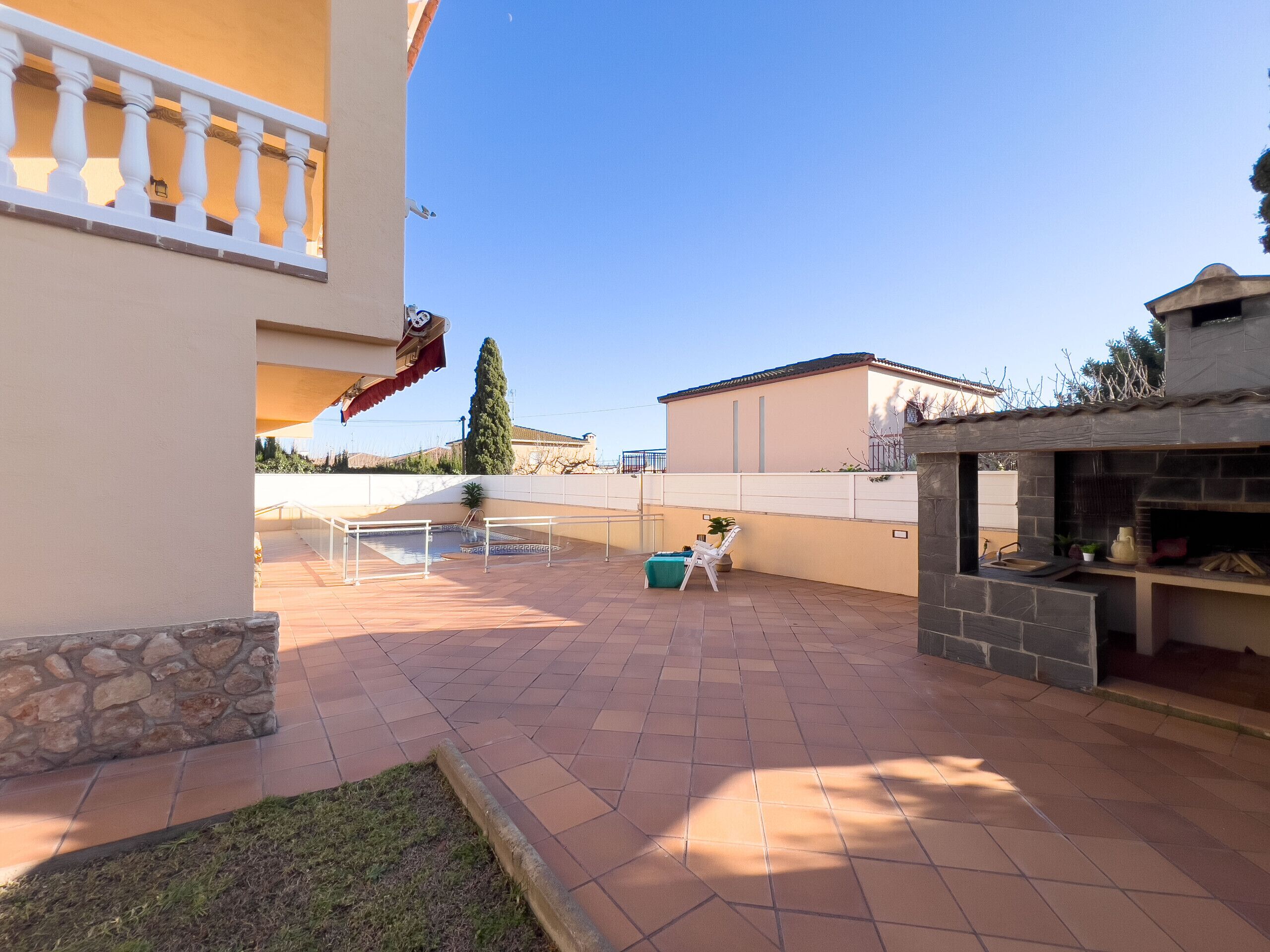 A patio with a stone wall, a pool, and a barbecue area.