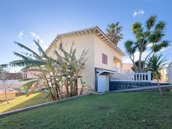Une maison à deux étages dotée d’un balcon, entourée d’une pelouse bien entretenue et de palmiers.