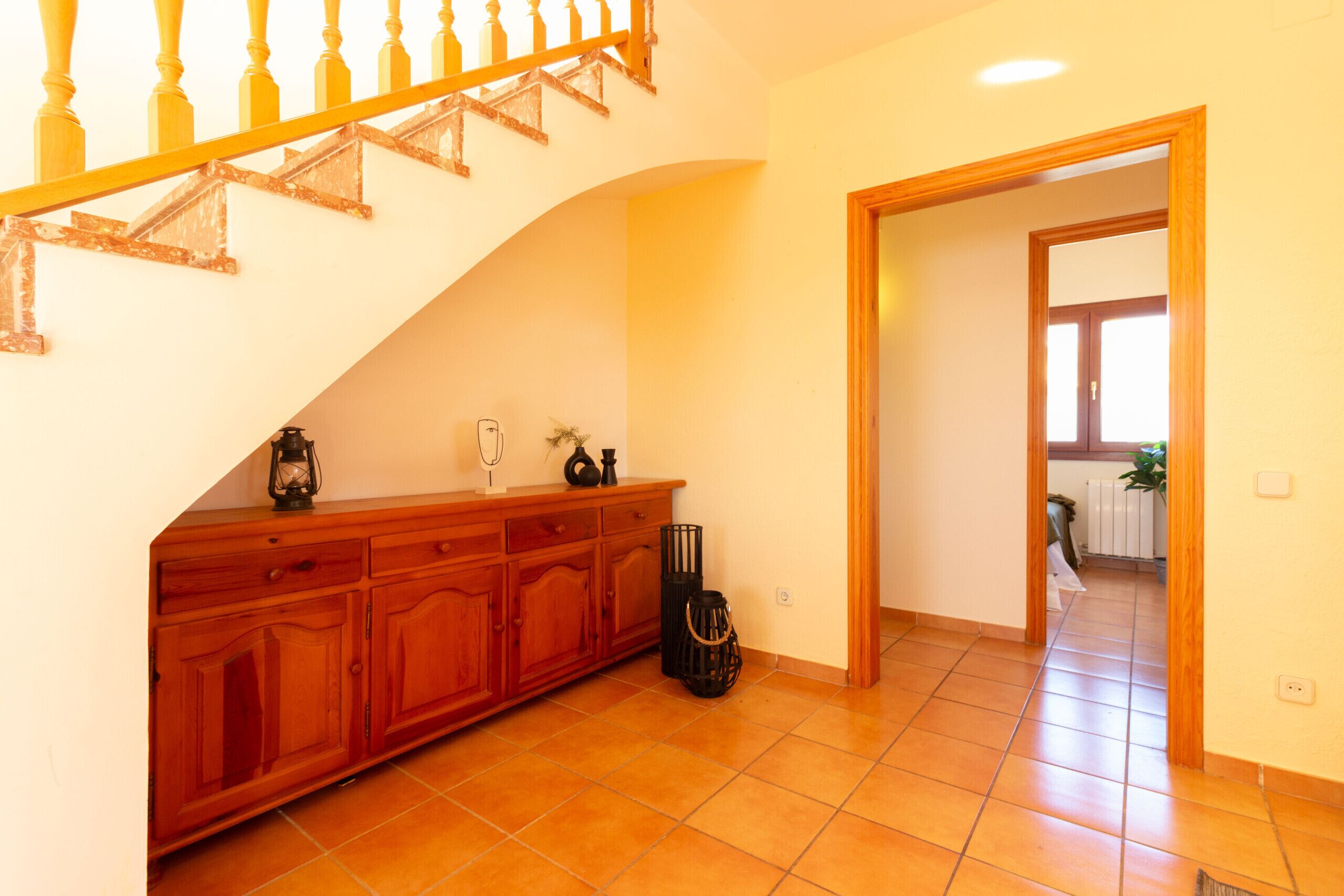 A staircase with wooden balusters, a wooden cabinet with drawers, a black metal basket, and a tiled floor.
