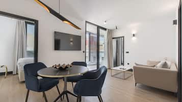 Una sala de estar moderna con una mesa redonda, dos sillas azules, un sofá beige y un televisor montado en la pared.