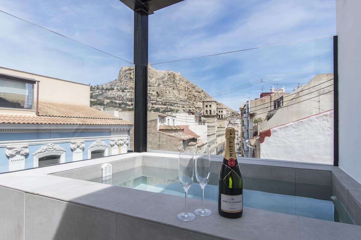 Un balcón con una botella de Moët & Chandon y dos copas, con vistas a un paisaje montañoso que incluye edificios.