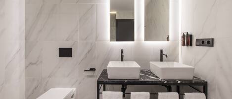 A modern bathroom with two sinks, a toilet, and a mirror.
