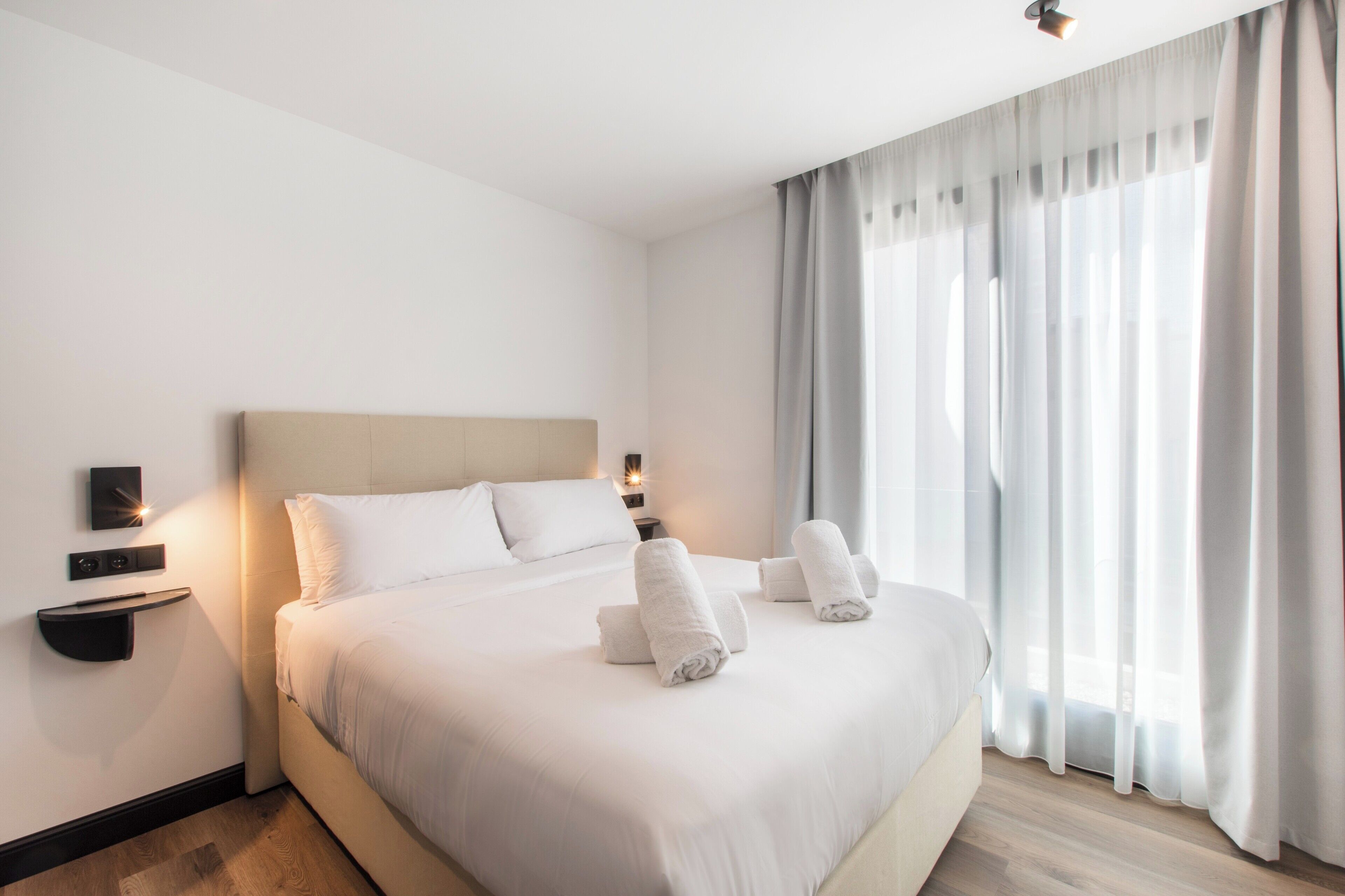 Une chambre d’hôtel avec un grand lit, deux tables de chevet, un téléviseur fixé au mur et une fenêtre avec des rideaux.