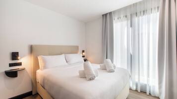 Une chambre d’hôtel avec un grand lit, deux tables de chevet, un téléviseur fixé au mur et une fenêtre avec des rideaux.