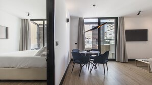 Una habitación de hotel moderna con una cama, una zona de comedor con sillas, una mesa y un televisor montado en la pared.