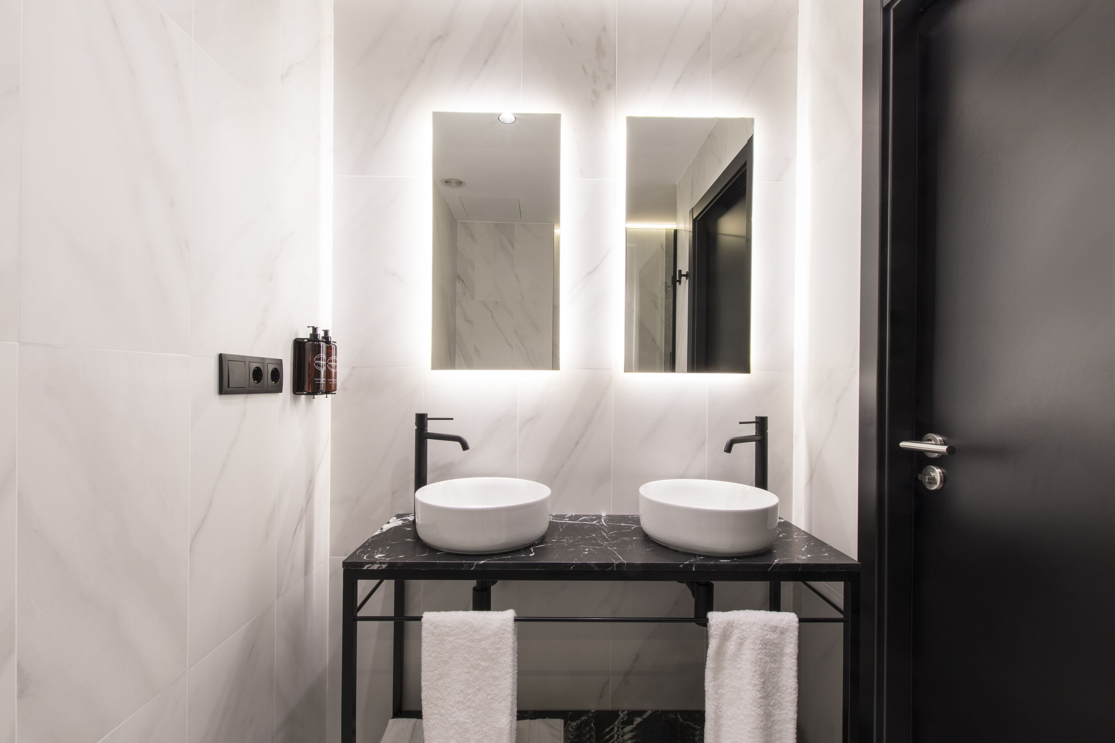 Un baño moderno con dos lavamanos, una encimera negra y un espejo grande.