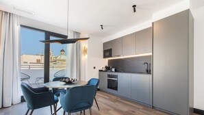 Una cocina moderna con armarios grises, horno empotrado y microondas. Cuenta con un comedor con una mesa redonda y sillas azules.