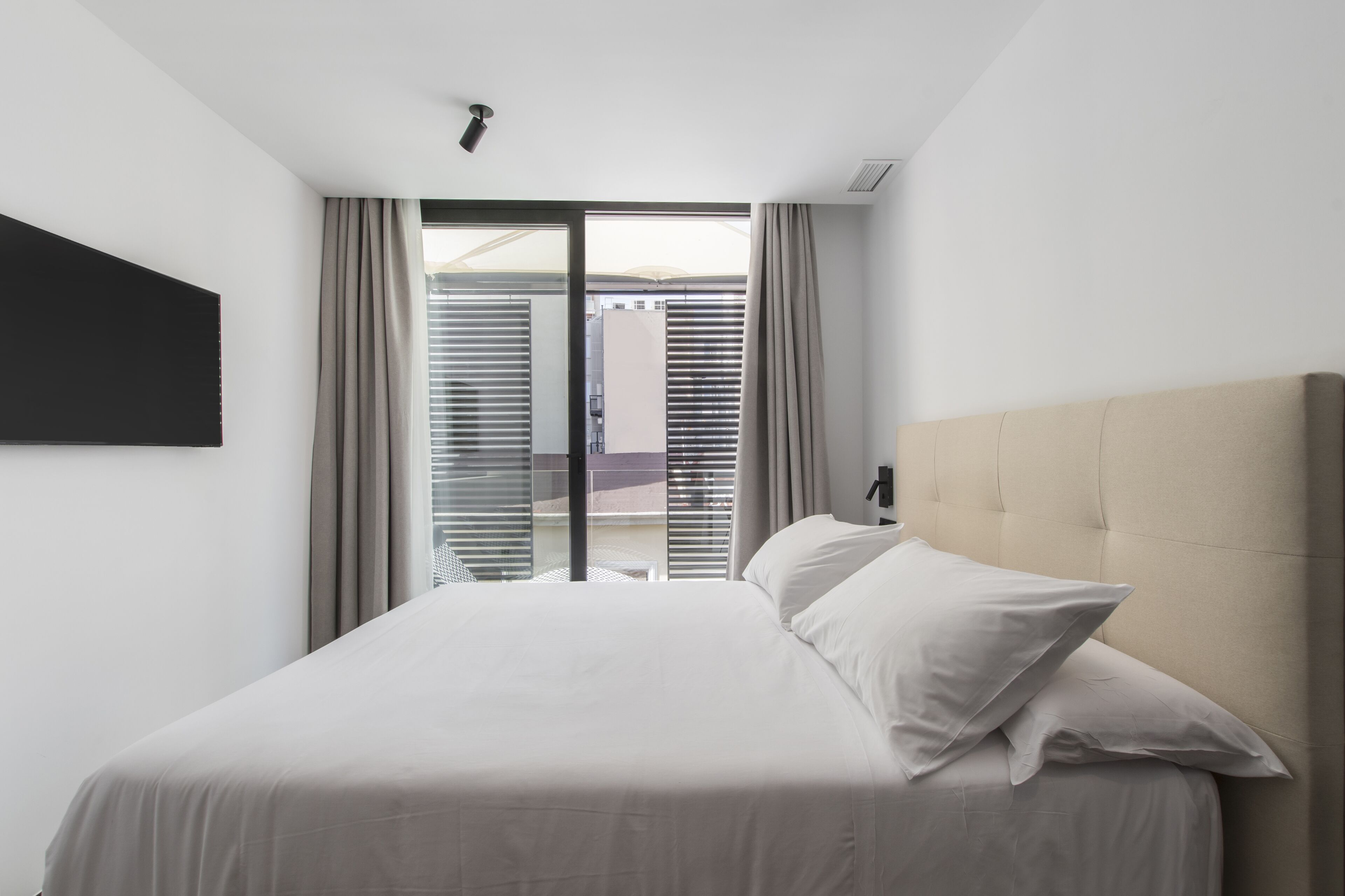 A modern hotel room with a large bed, a flat-screen TV mounted on the wall, and a sliding glass door leading to an outdoor area.