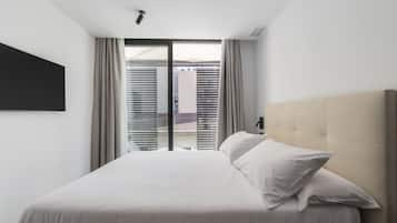 A modern hotel room with a large bed, a flat-screen TV mounted on the wall, and a sliding glass door leading to an outdoor area.
