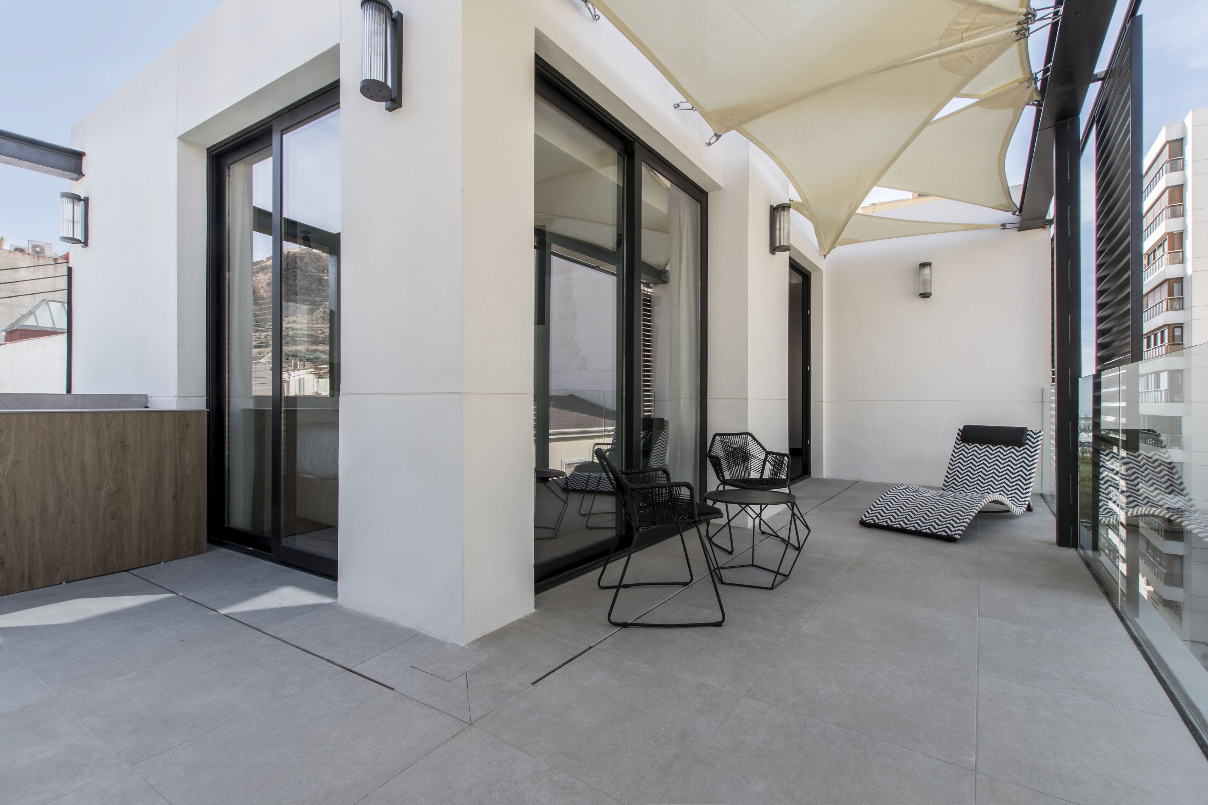 Une terrasse extérieure moderne avec des portes vitrées, un espace salon couvert et un fauteuil de détente.