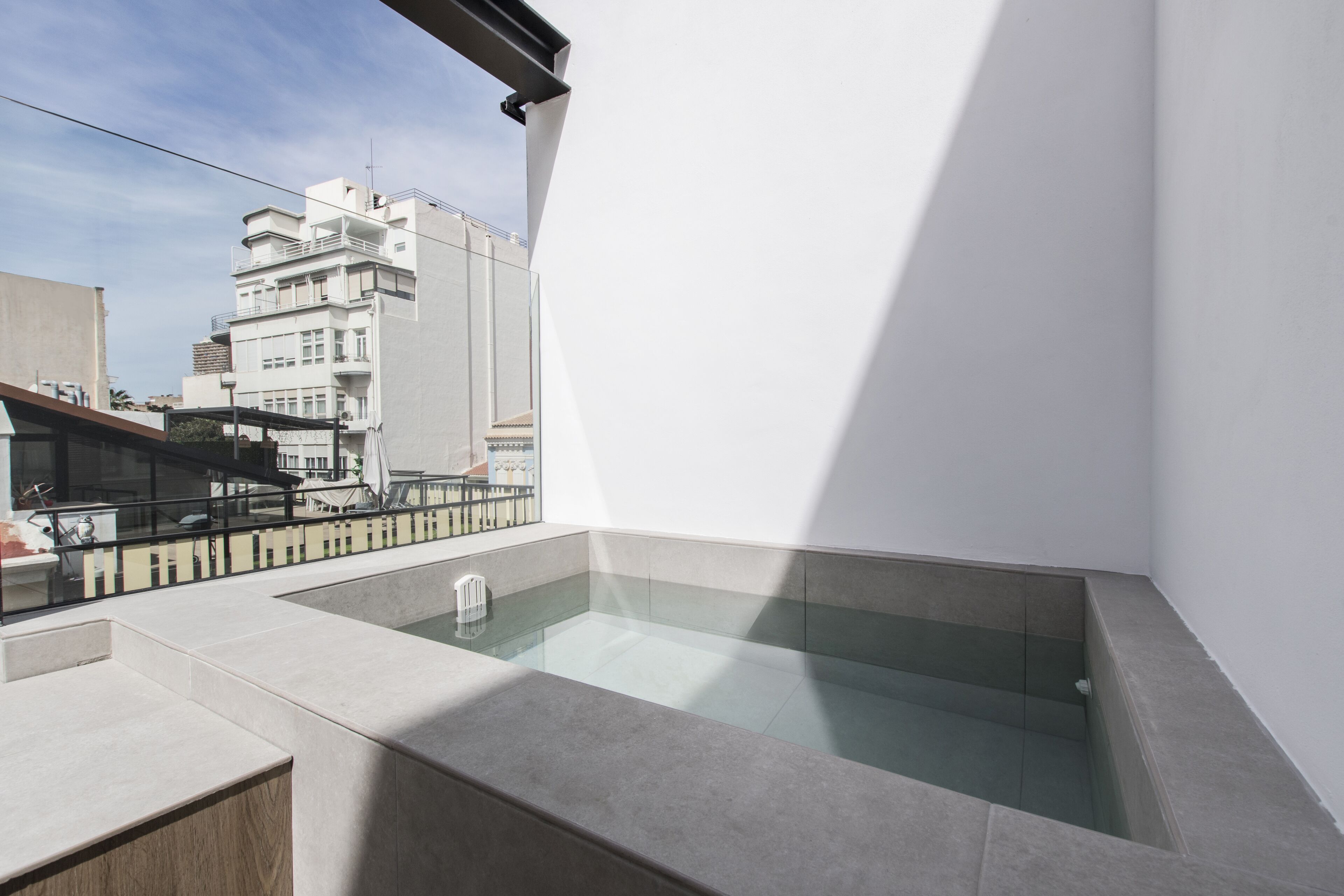 Una terraza moderna en la azotea con un jacuzzi cubierto de vidrio, un área de estar y vistas a la ciudad.