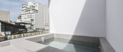 Una terraza moderna en la azotea con un jacuzzi cubierto de vidrio, un área de estar y vistas a la ciudad.