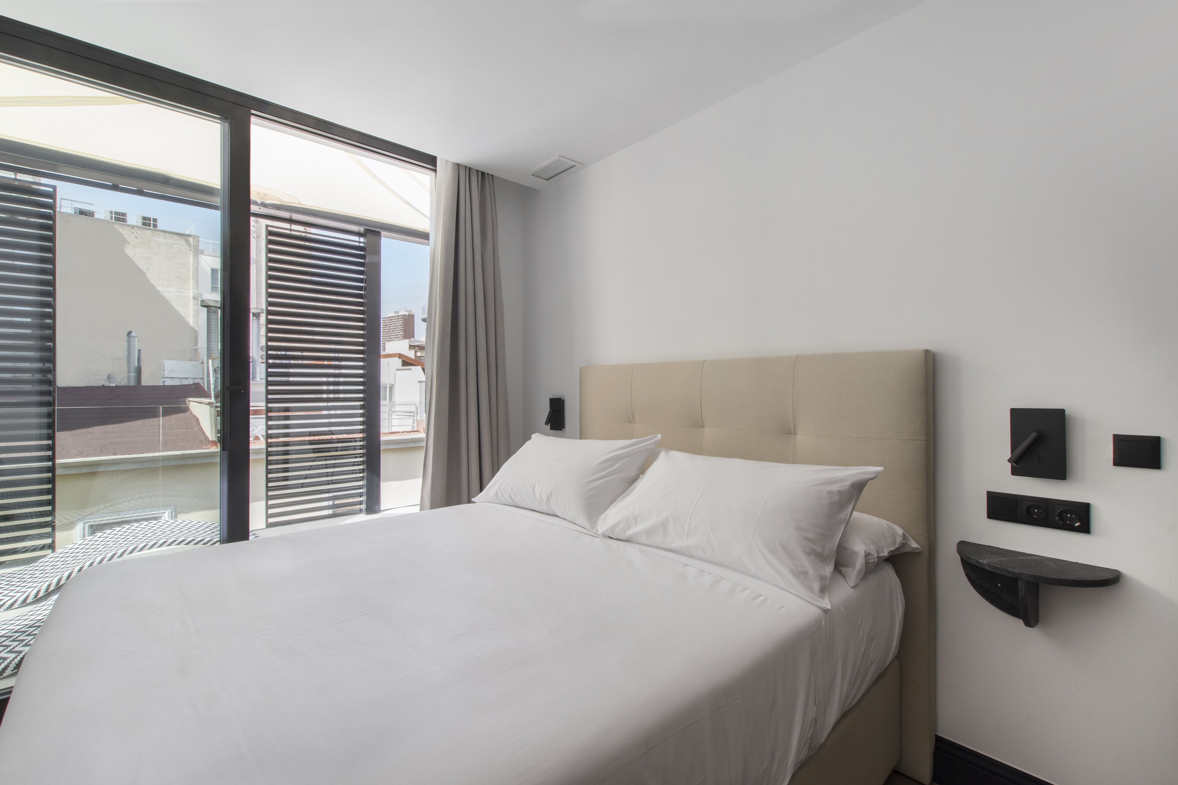 Una habitación de hotel moderna con una cama grande, una puerta corredera de vidrio al balcón y un diseño de pared minimalista.